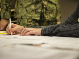 A Navy recruit signing an enlistment contract at a MEPS office