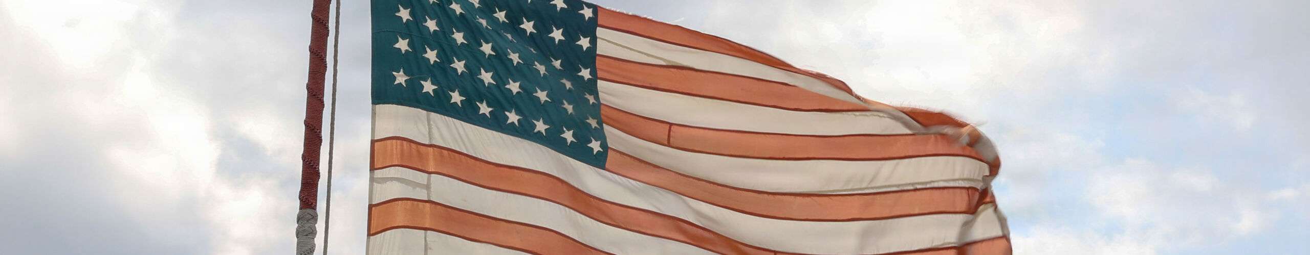 A 48-star flag made out of parachutes by American POWs who survived the Bataan Death March flies over the Wasp-class amphibious assault ship USS